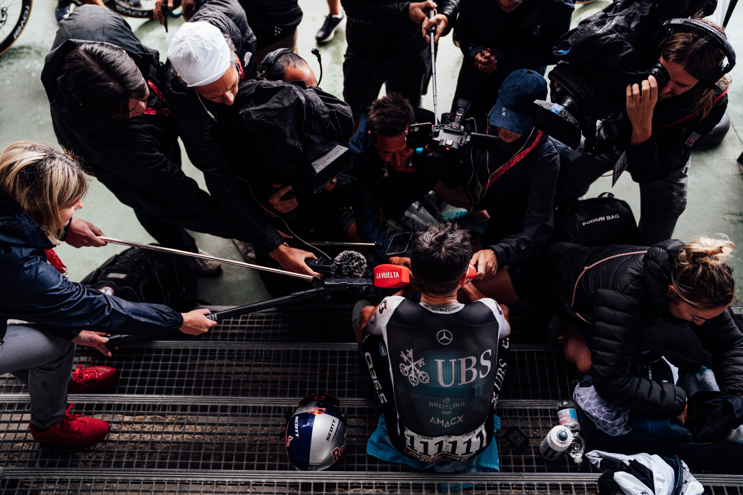 Tom Pidcock surrounded by media and microphones during a post-stage interview.